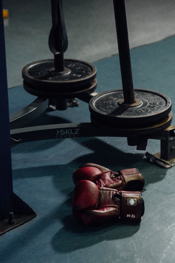Boxing gloves on a gym floor beside a weights rack